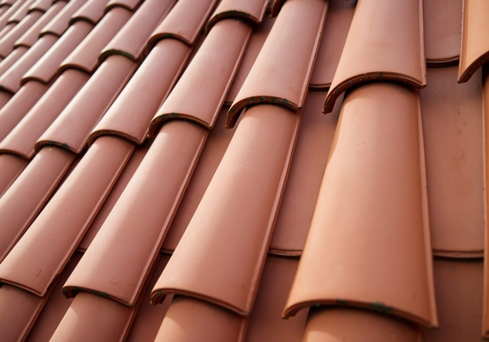 Red ceramic roof tiles covering residential building roof. Tile pattern close-up